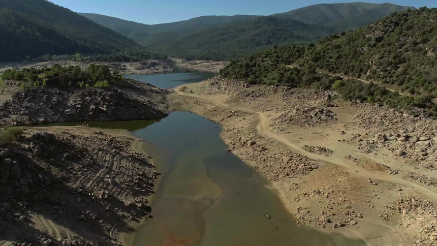 A dirt road runs by the side of a body of water in a valley
