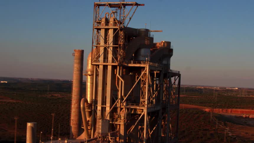 A tall factory with multiple smokestacks in the countryside during the day