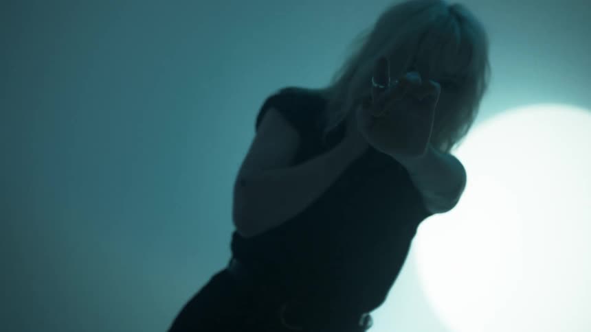 A young white woman extends her hand and fingers while moving about in front of a projection screen