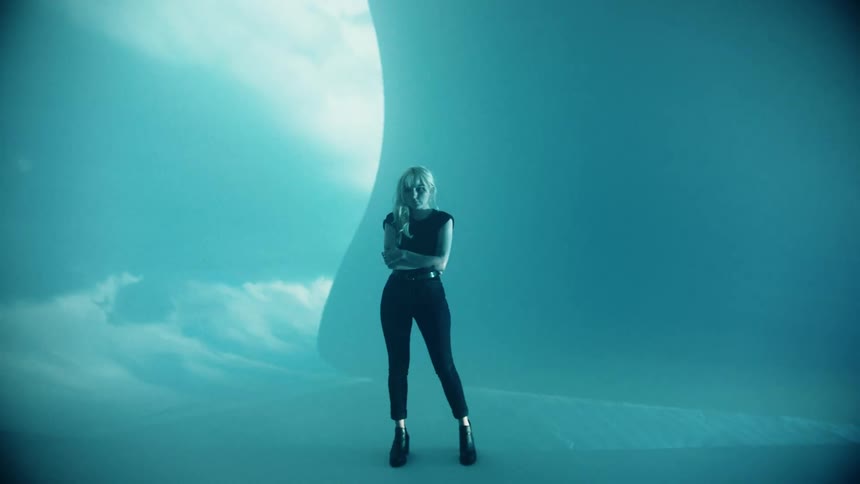 A white woman dressed in black stands in front of a projection screen