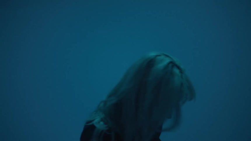A white woman paces about in front of a giant projection screen