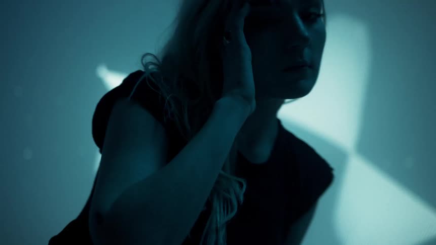 A white woman moves in front of a giant screen with images flashing on it