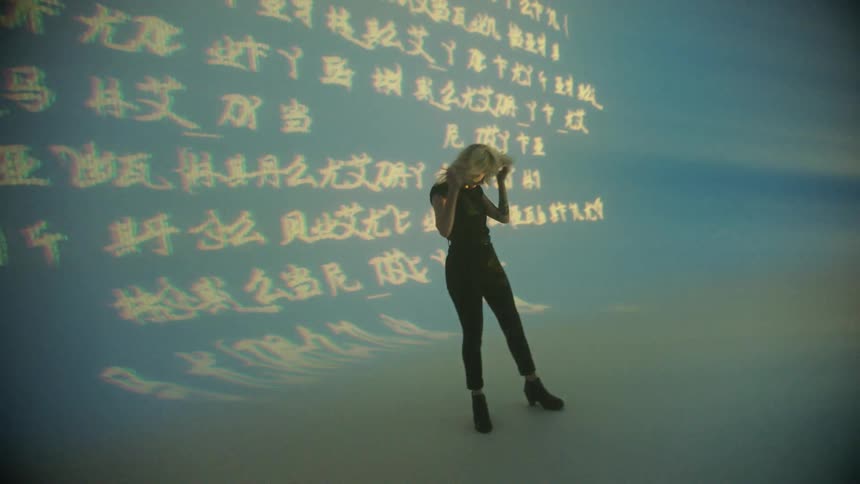 Spotlight shines on a woman on stage as a text graphic is behind her