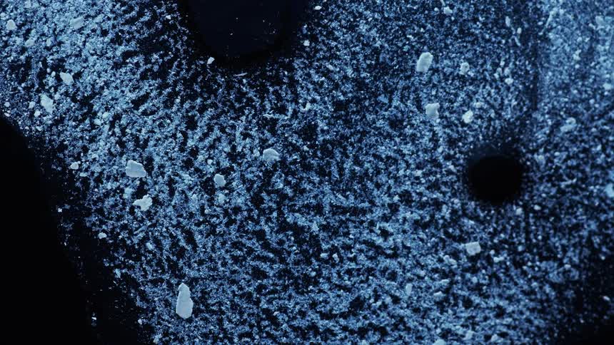 A blue liquid flows and swirls on a black surface