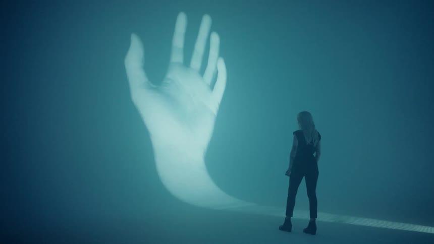 A woman standing looking at a projection of a hand on the wall