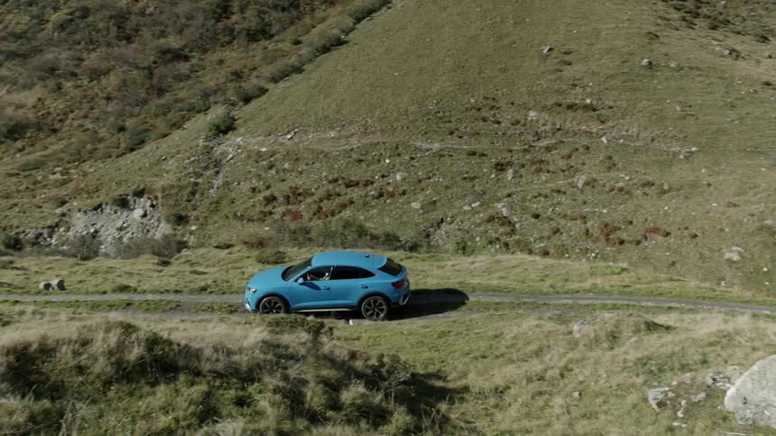 Blue suv drives down dirt road in rugged landscape