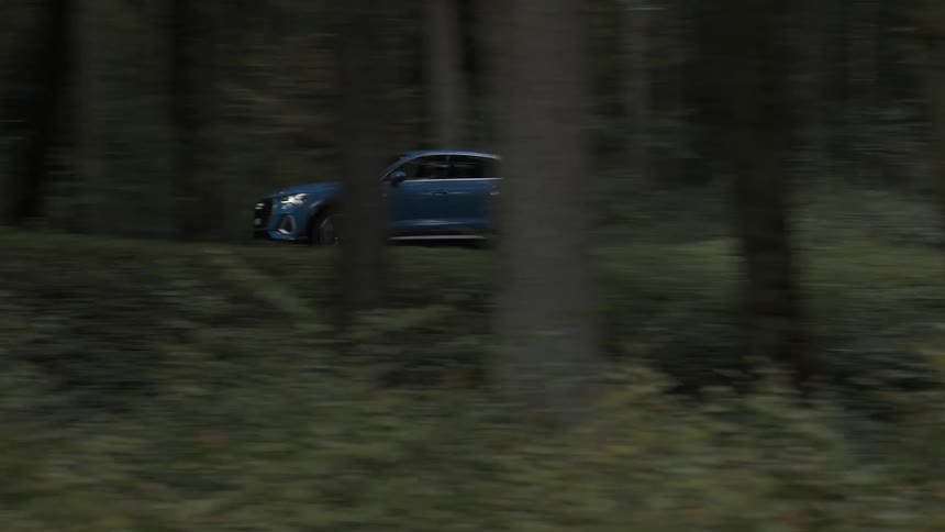 A blue car drives down a road that goes through a forest