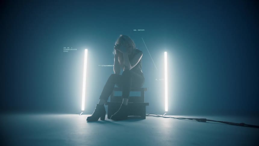 Young woman sits on stool in front of lights and projected image of text