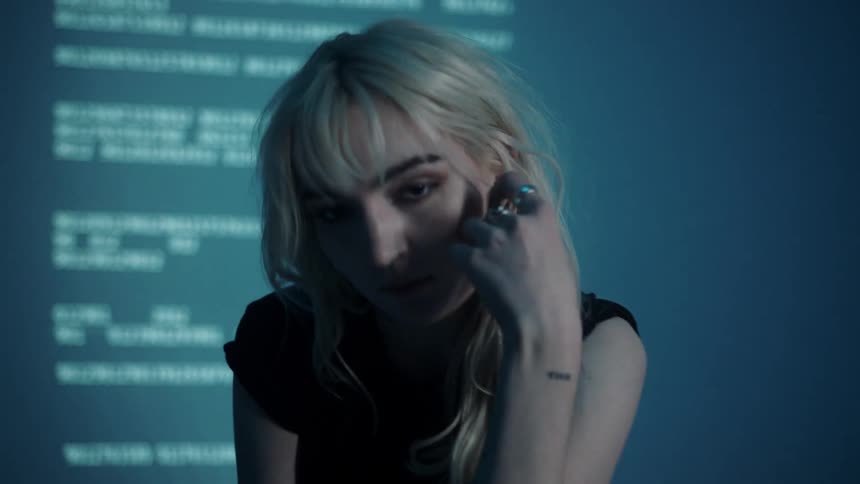 Young woman poses for camera in front of projected blurred text in dark room