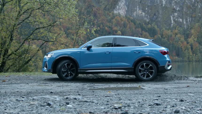 A blue sport utility vehicle turns around through a muddy puddle near a mountain lake