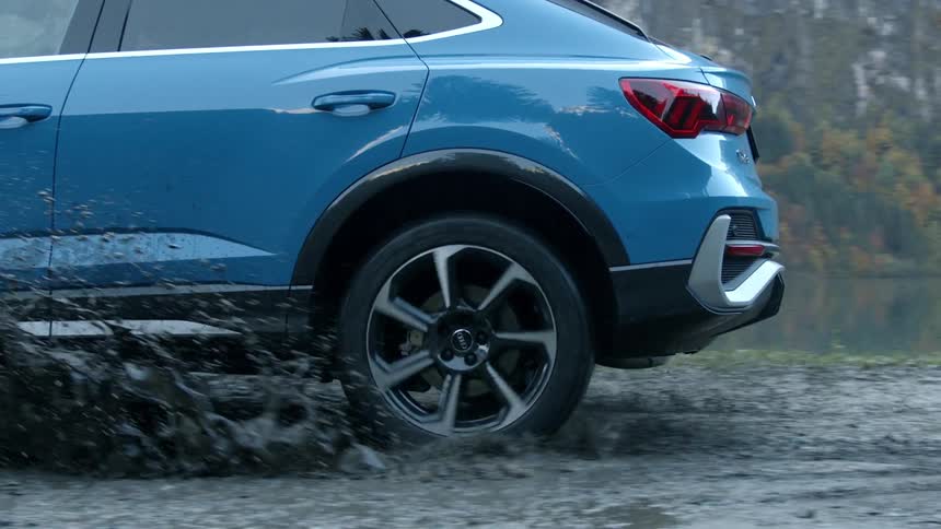 A car splashes through a muddy puddle on a dirt road in the hills