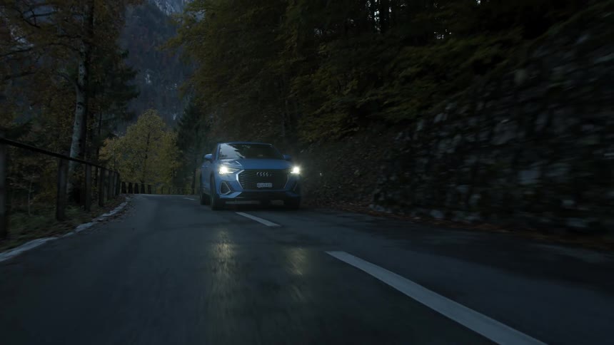 A car with headlights on travels alone on a mountain road