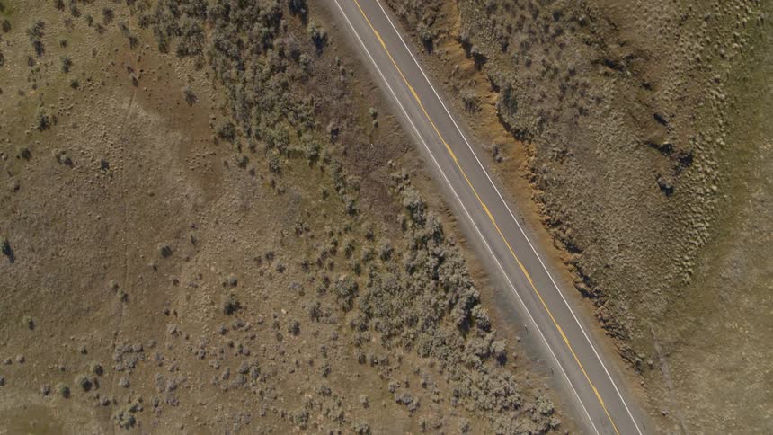 Top down view of an empty two lane highway running through sagebrush covered foothills