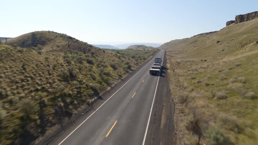 A semi truck and trailer travels along an open road through rolling hills