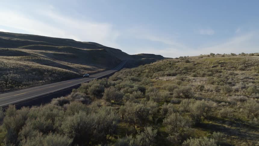 Pullback traverse over sagebrush as a car drives by on a rural country road