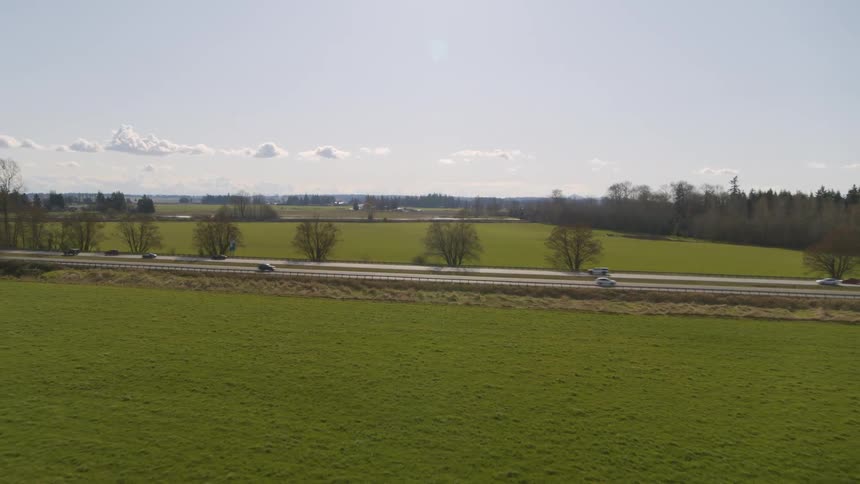 Vehicles drive along an interstate highway surrounded by green farm fields