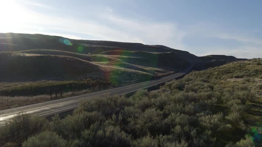An empty road stretches through the hills and brush on a bright sunny day