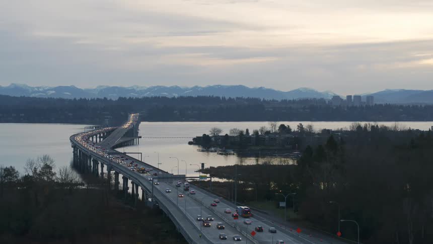Traffic flows along a highway with mountains and the skyline of a city in the distance