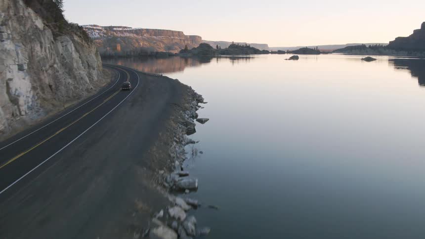 Fast chase behind a black pickup truck as it drives down a rural highway next to a lake and rugged cliffs