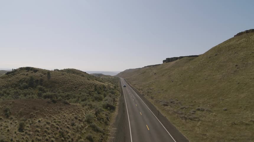 Pivot around a rural road through rolling hills as a dark blue SUV drives through frame