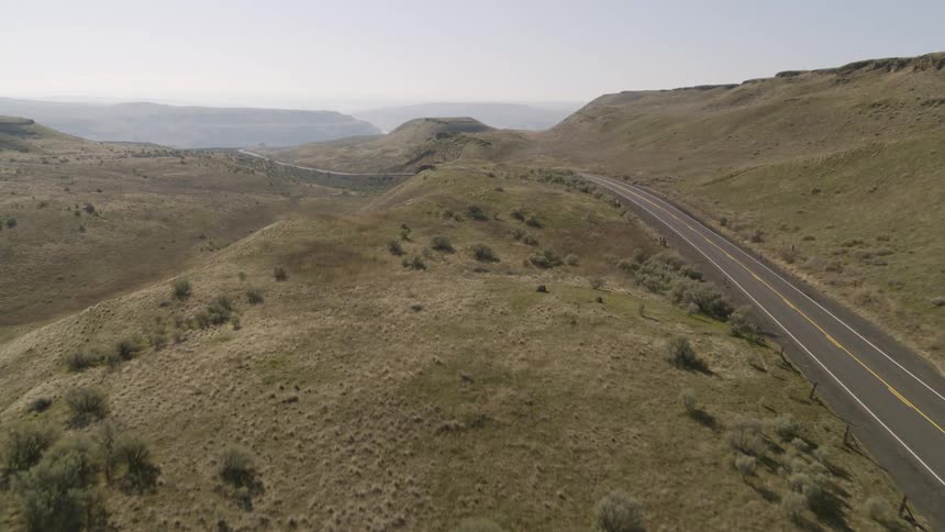 Wide pullback traverse along an empty two lane road running through rolling green grasslands