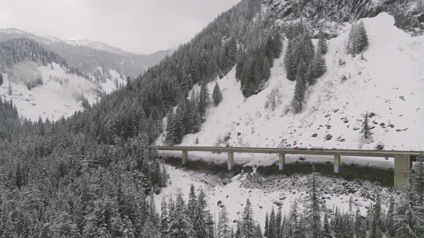 A double tanker semitrailer drives across a bridge through snow covered mountains