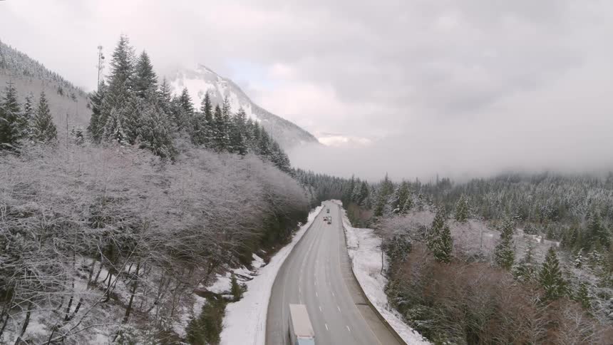 Semi trucks travel along a frosty mountain pass highway surrounded by snow covered trees