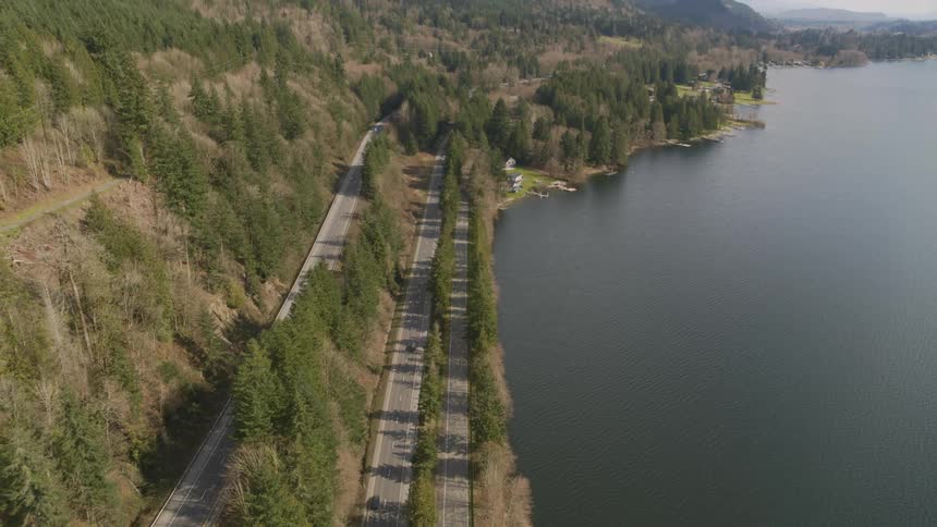 Pullback tilt up traverse of vehicles driving on a lakeside interstate highway