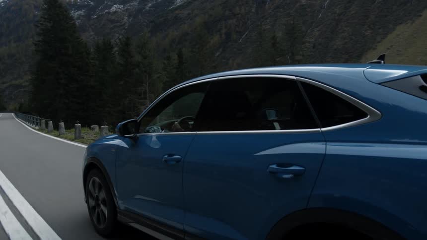 A blue car travels on an empty mountain road