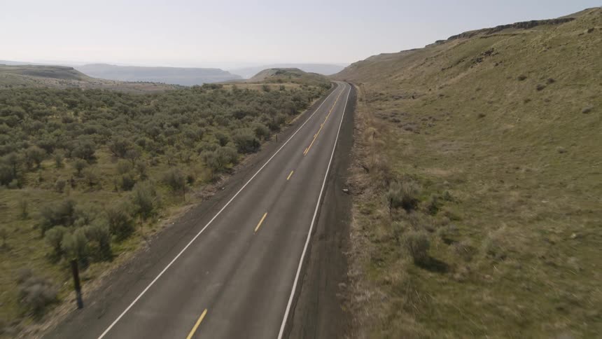 Low pullback traverse over an empty two lane highway traveling through a rugged landscape