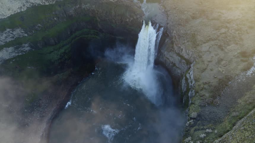 Birds eye view of a misty waterfall flowing over a rocky canyon cliff