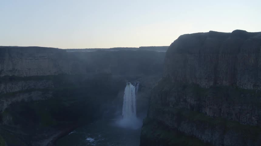 Moving slowly upstream toward a waterfall in a rugged rock canyon at first light