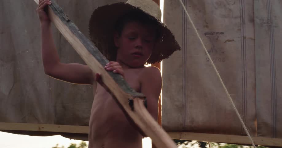 A young boy uses a piece of wood to paddle a handmade boat in a developing nation river