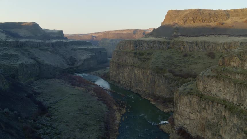 Flying above a winding river channel within a deep and narrow rock canyon