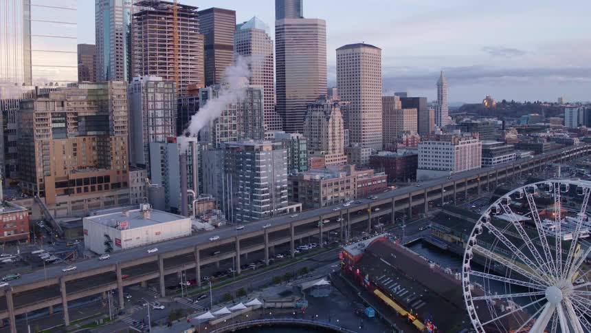 Cars travel on a multi level highway between a city skyline and waterfront with a ferris wheel