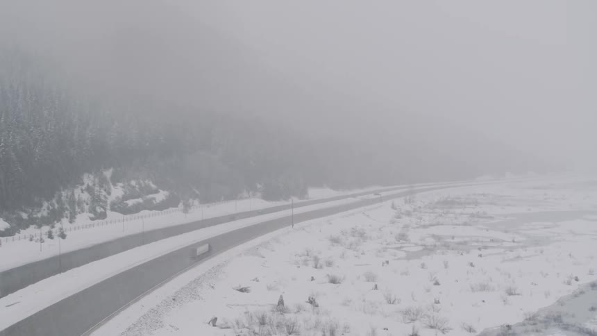 A winter storm dumps heavy snow on vehicles traveling on a mountain pass highway