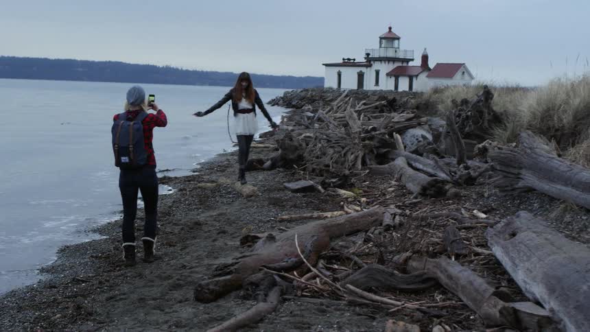 Woman taking photo of friend on shore in front of lighthouse