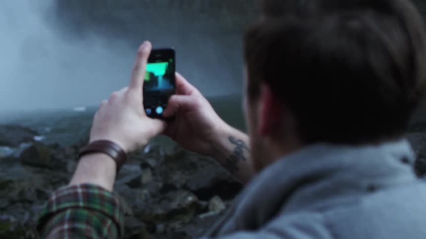 Man uses cell phone to take photo of waterfall
