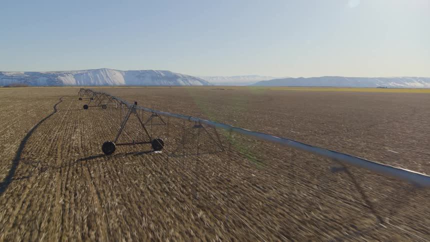 Revealing an enormous field of tilled farmland with blue mountain cliffs in the far distance