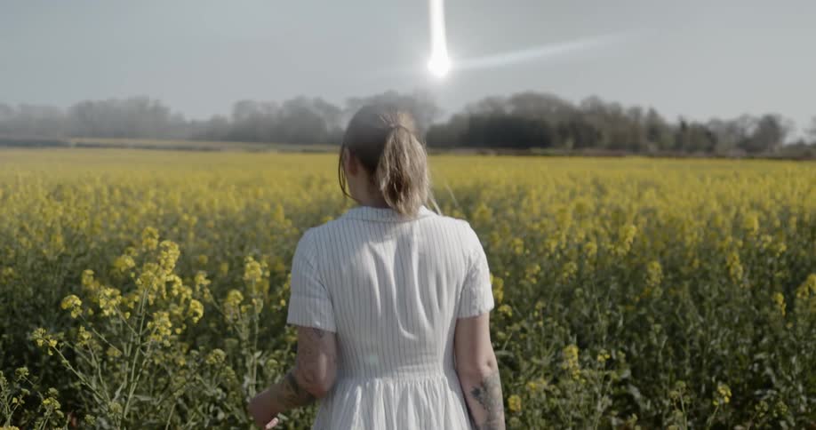 A woman wearing a white dress walks through a field of wildflowers