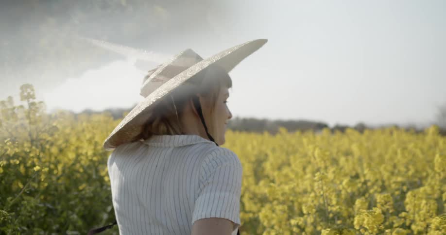 Woman wearing large straw hat running through field of yellow flowers and laughing