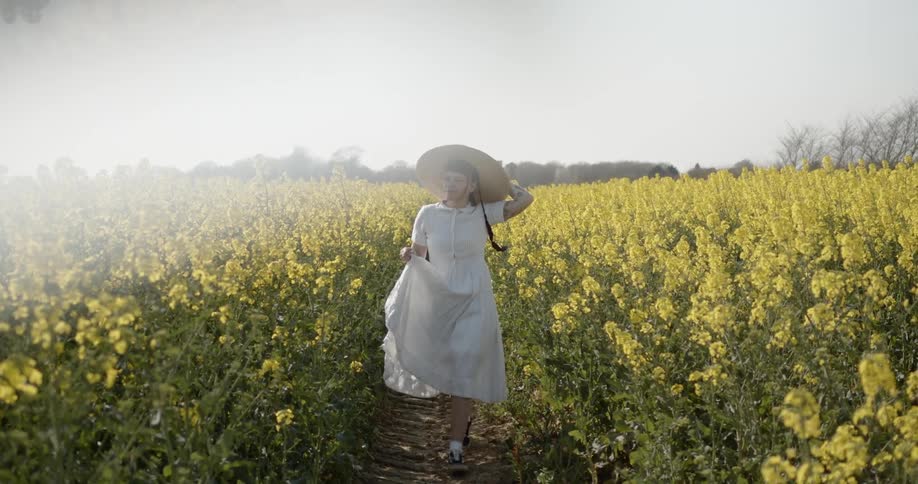 A woman with a hat walking through a field of flowers