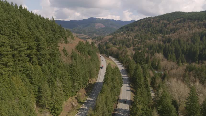 Vehicles driving along a four lane divided highway through the mountains in early spring