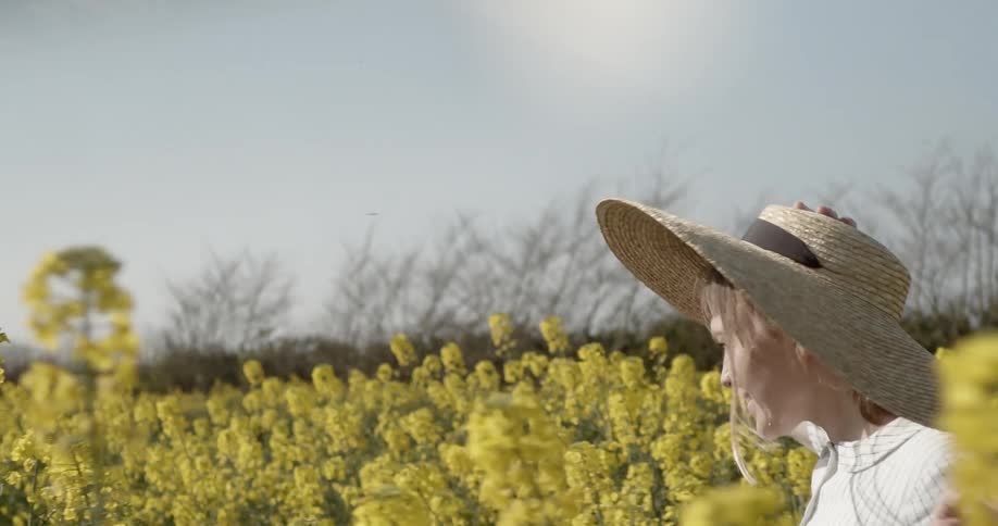 Young woman in straw hat runs through field of yellow wildflowers laughing