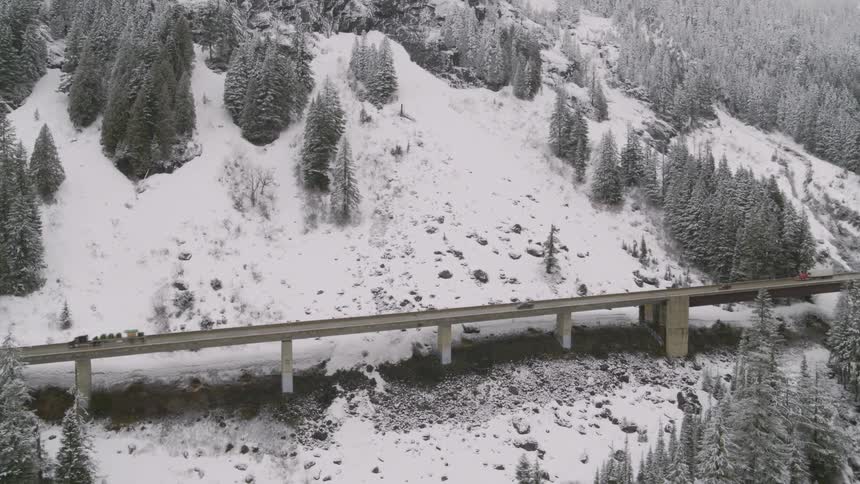 Traffic drives over an elevated interstate highway on the slope of a snowy mountain