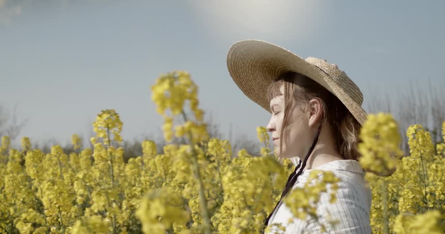 A woman in a straw sunhat walks in a meadow of yellow flowers