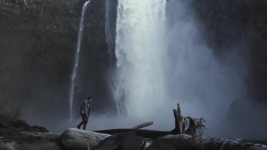 The man walks in front of the waterfall