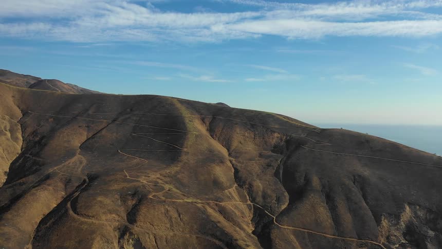 A ridge with tracks and roads and ocean behind on a bright blue sky day