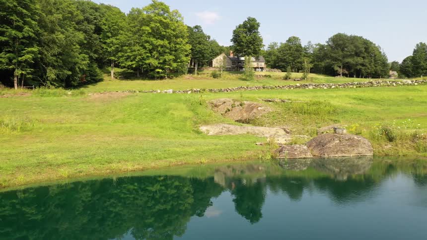 House in a field close to the trees near the calm waters of a lake