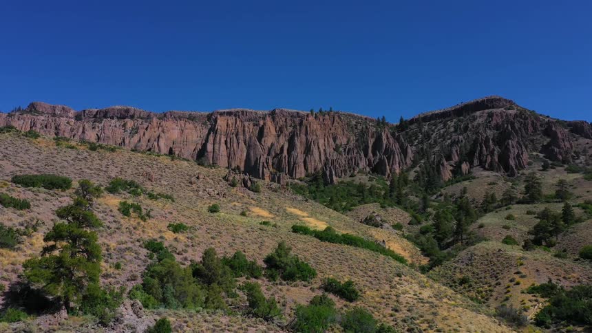 Cliffs loom over hardscrabble land dotted with trees and scrub